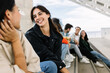 © Xavier Lorenzo - Portrait of two young multiracial women hanging out sitting outdoors with diverse friends. Friendship and bonding concept