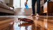 © David Zarzosa - Man spraying insecticide on a cockroach crawling across a wooden floor during pest control at home.