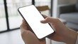 © Husen - Close-up of a person's hands holding and using a smartphone with a blank white screen for mockup purposes.