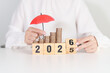 © Jo Panuwat D - 2025 end year to Happy New Year 2026 with hand holding red umbrella and money stack growing. Insurance, protection, safety and New year holiday Concepts