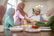© Art_Photo - Muslim big family sharing traditional meal together around dining table wearing hijabs and kufi in cultural love, ramadan iftar celebration, eid al-fitr festive, halal meal gathering food culture