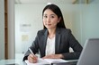 © Aliaksandr Barouski - Professional businesswoman sits at a desk, writing notes in a modern office.