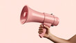 © MD - Hand holding a pink megaphone against a soft peach background