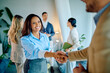© we.bond.creations - Smiling young businesswoman shaking hands with a male colleague, finalizing a successful business deal in a modern office