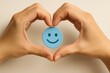 © emi numa - ハートの手で包む青いスマイルアイコンの幸福イメージ/Happy blue smile icon held by hands forming a heart shape