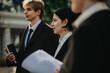 © qunica.com - A group of colleagues in suits stand outside, holding papers and notebooks, engaged in a focused discussion.