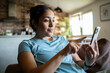 © Marko Geber - Young adult woman relaxed and focused on smartphone at home