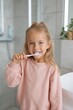 © Ilia K - Little girl brushes her teeth in a bright bathroom, enjoying her morning routine with a big smile