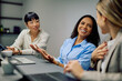 © we.bond.creations - Multiracial businesswomen collaborating, discussing, and smiling during a professional meeting in a modern office environment