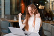 © Iryna - Young woman celebrates success while using laptop at outdoor cafe in a vibrant city setting