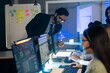 © winnievinzence - Manager, reviews data and reports on a computer screen, overseeing a diverse team in a high-pressure at command center or control room. executive is providing critical guidance on an urgent late night