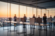 © f_bossa - Silhouettes of people standing at desks in a modern office with large windows overlooking a city skyline at sunset.