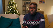 © ABCreative - A young man of multi-ethnic background sits on a sofa in the living room. His mother called to wish him Merry Christmas. He is talking happily, smiling on the phone, and glad to hear her voice.