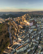 © AmazingAerialAgency - Aerial view of the charming town cascading down the hillside, bathed in warm light, contrasting with the cool shadows, Calitri, Irpinia, Italy.