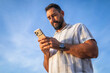 © Lupe Rodriguez/Stocksy - Bearded man using smartphone with blue sky background