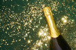 © Basil Pind/Stocksy - Champagne bottle on green surface with golden glitter