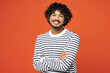 © ViDi Studio - Young smiling happy cheerful fun Indian man he wear striped sweatshirt casual clothes hold hands crossed folded look camera isolated on plain red orange background studio portrait. Lifestyle concept.