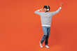 © ViDi Studio - Full body young smiling happy Indian man he wear striped sweatshirt casual clothes listen to music in headphones raise up hands dance isolated on plain red orange background studio. Lifestyle concept.