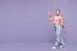 © ViDi Studio - Full body young shocked surprised happy woman wear pink tank top casual clothes walk go point index finger aside overhead on area isolated on plain pastel light purple background. Lifestyle concept.