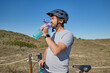 © Anna Baranova - Man wearing a helmet drinking water from a bottle during a cycling break in nature.