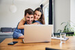 © baranq - Young couple hugging while shopping online using laptop at home