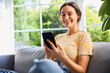 © baranq - Cheerful young woman using mobile phone sitting on sofa at home