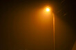 © Олег Струс - A bright orange streetlight on a tall pole pierces through thick fog or haze on a dark night. The light creates a halo, giving the scene a mystical and enigmatic appearance.