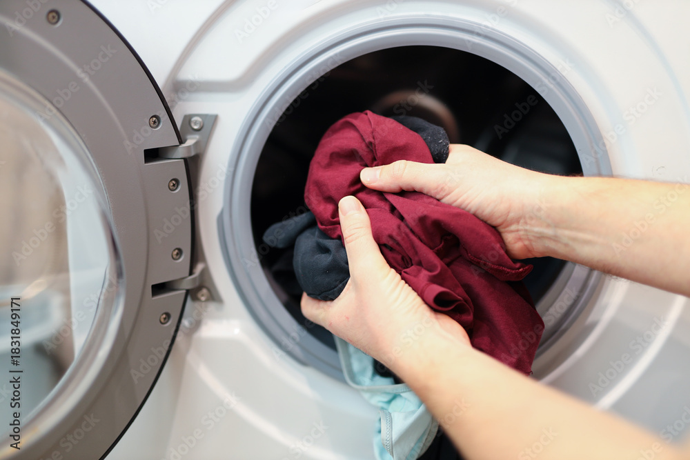 Hands loading laundry into washing machine with colorful clothes ...