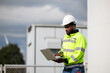 © NVB Stocker - African Engineer man working on tablet computer in field with wind turbines background, Windmill. environmental renewable clean energy. Wind power generation. Windmill engineer inspection progress