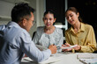 © Crystal - Young Asian businesspeople discussing project details and calculating figures while working late in a dark modern office