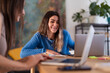 © Studio Marmellata - Two women collaborate on a project, smiling as they work together on laptops and review notes at a wooden desk.