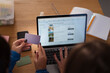 © Studio Marmellata - A person holds a payment card while booking a hotel online on a laptop, with another card visible on the desk.