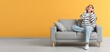 © Pixel-Shot - Happy woman in headphones sitting on comfortable sofa near yellow wall. Banner for design