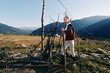 © SHOTPRIME STUDIO - Woman hiking in mountains and nature across a rural meadow, walking with a wooden stick near a rustic fence. Portrait travel scene with sunlight, valley landscape and peaceful exploration.