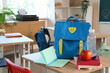 © Pixel-Shot - Blue backpack with apple, water bottle and books on desk in classroom