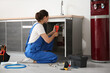 © Pixel-Shot - Female plumber with pipe wrench fixing sink in kitchen