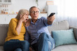 © Prostock-studio - Couple sits on a comfortable sofa, sharing a joyful moment while watching a movie. They are engaged and surprised, holding a remote control.