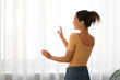 © Pixel-Shot - Young woman near curtains at home, back view