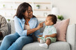 © Prostock-studio - An African American mom smiles as she plays with her cute baby on the couch. They enjoy a happy moment, sharing laughter while bonding in their comfortable living room at home.