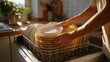 © imagemir - A man places clean dishes in a kitchen dishwasher, showcasing a cozy and sunlit kitchen atmosphere.