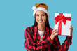 © Pixel-Shot - Beautiful young woman in checkered pajamas and Santa hat with gift box on blue background. Christmas celebration