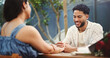 © peopleimages.com - Couple, holding hands and happy on date at restaurant with bouquet, discussion and relationship milestone. Man, woman and smile for connection with bonding, trust or flowers on anniversary at diner