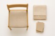 © Artcuboy - Top view wooden chair next to neatly folded beige throw blanket and small stack of hardcover books all arranged on bright white background
