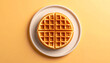 © Fawitra - Overhead shot of a golden waffle on a white plate against a yellow background.