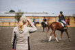 © encierro - Horse trainer instructing riders  before equestrian jumping event. Woman animal instructor focused on horseback riding in paddock
