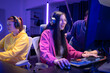 © Wosunan - Group of woman play online game and celebrating a gaming victory in a neon-lit room,