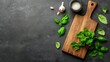 © Nally - Overhead shot of a wooden cutting board with fresh basil leaves, garlic, and salt on a dark textured surface.