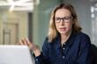 © Liubomir - Young businesswoman with glasses experiencing confusion and frustration while having a video call on a laptop, gesturing during a remote meeting or online conversation in an office setting
