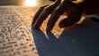 © JARVIS X - Closeup of a hand reading braille, illuminated by sunlight, promoting literacy for the blind and visually impaired, sensory exploration, education