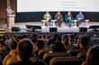 © Anton Gvozdikov - Panel of five speakers on stage during conference talk, audience listening intently in theater setting